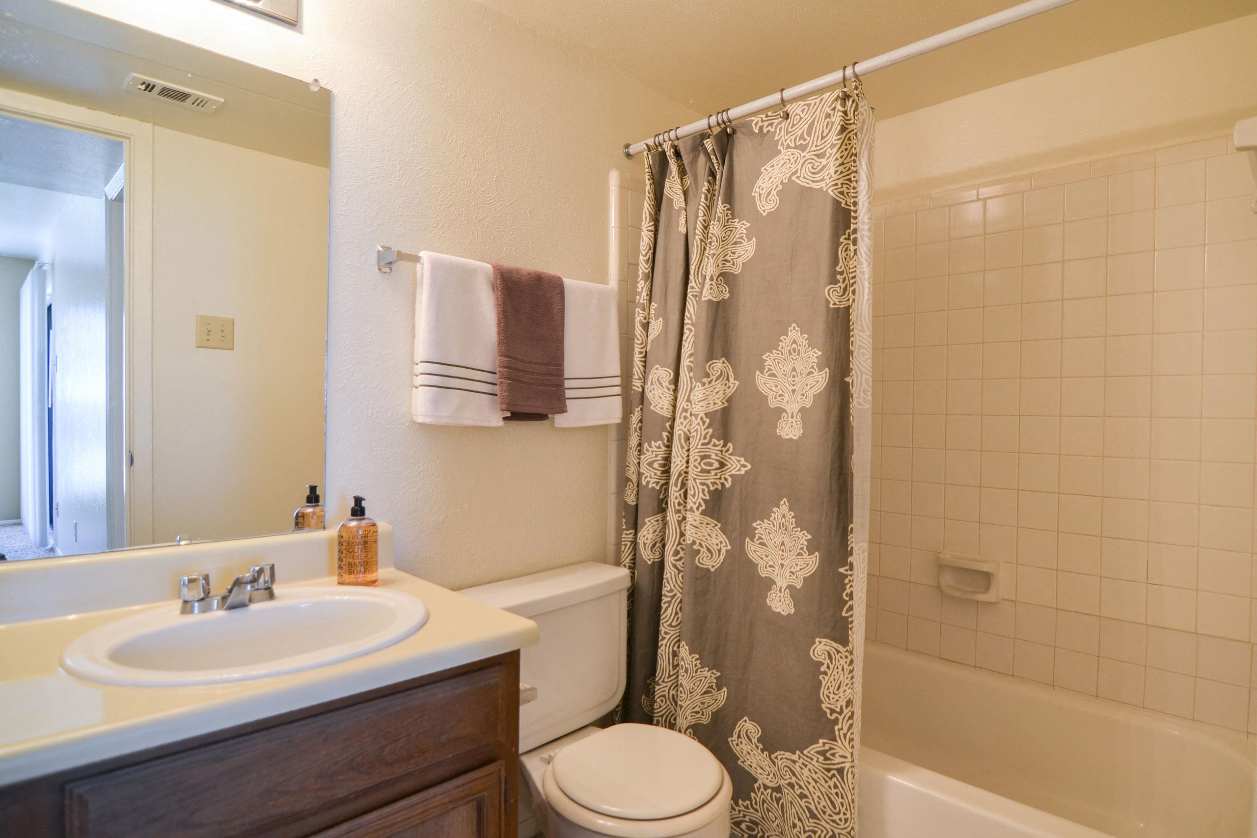 A bathroom with a tub, cabinet storage, and a wide mirror over the sink