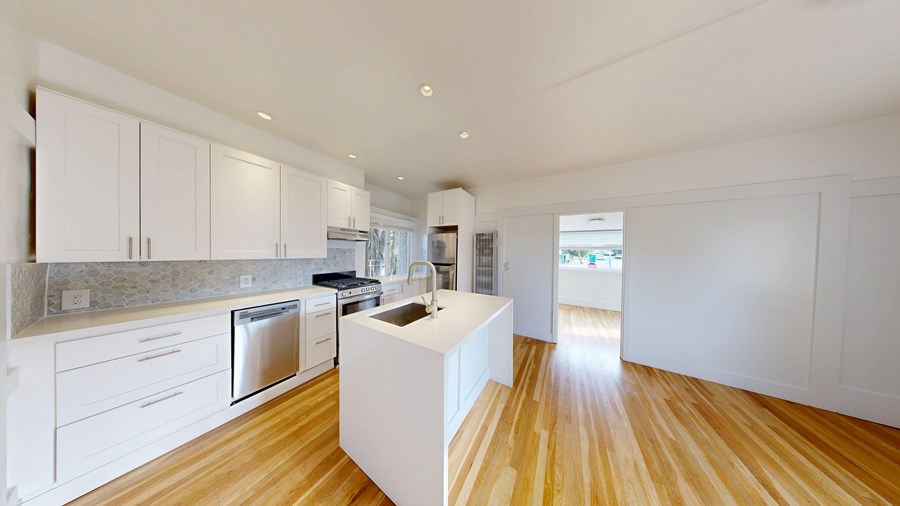 A modern kitchen with white cabinets and wooden floors.