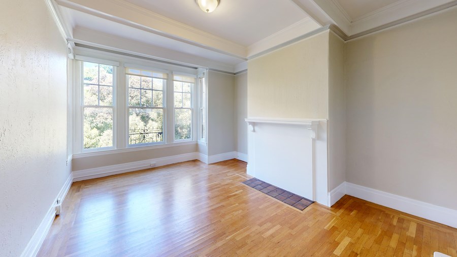 A room with wooden floors and a window overlooking trees.