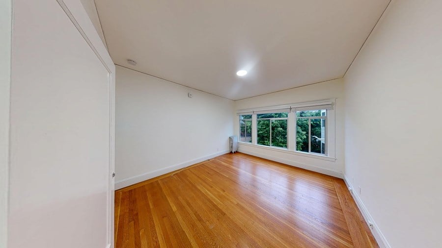 A room with wooden floors and a window with a view of trees outside.