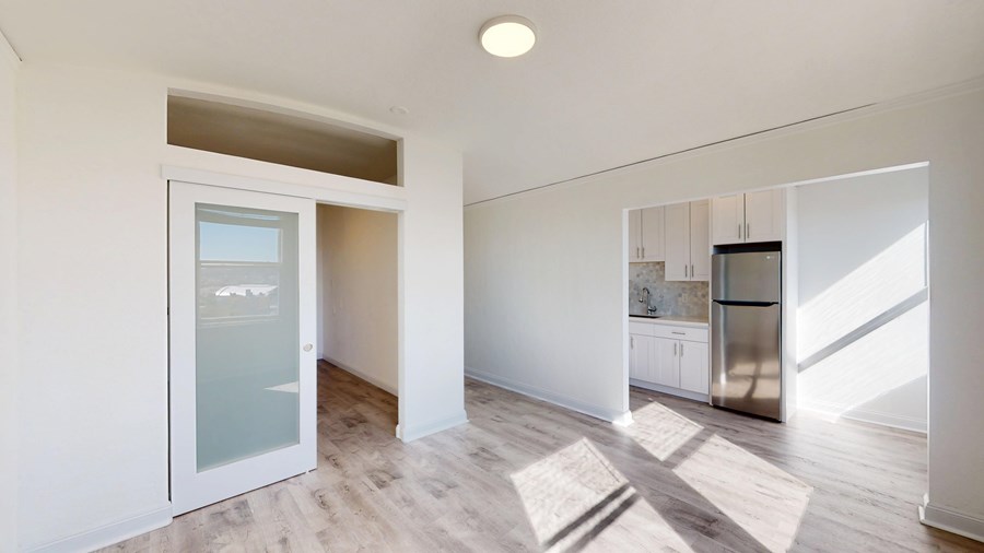 A kitchen with a refrigerator, microwave, and oven is visible through a glass door.
