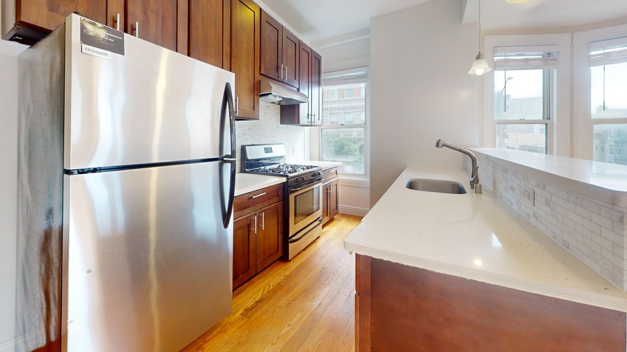 A kitchen with a stainless steel refrigerator and wooden cabinets.
