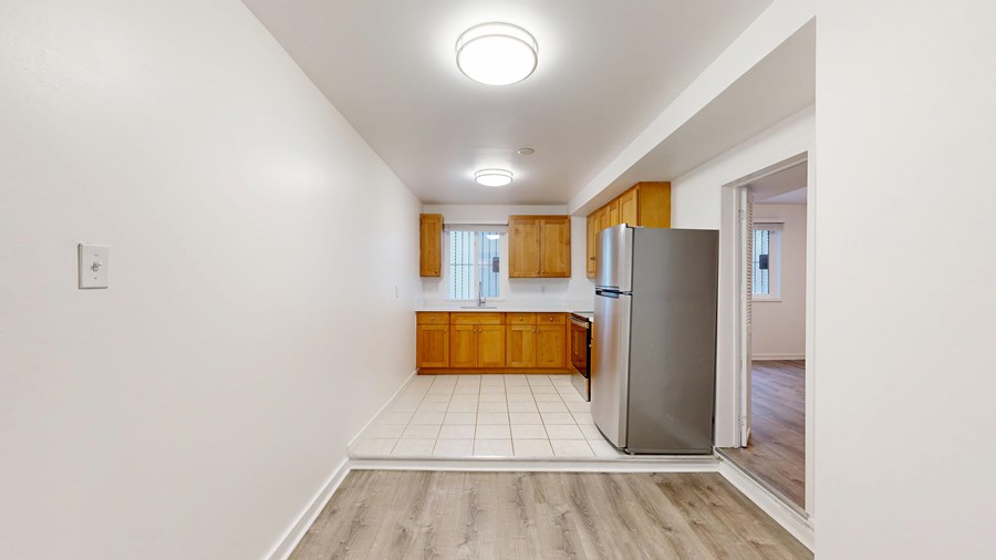 A kitchen with a refrigerator, wooden cabinets, and a window.