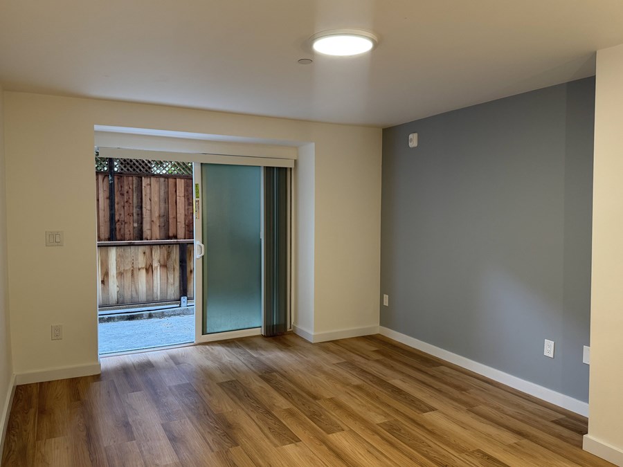 A room with wooden floors and a sliding glass door leading to a balcony.