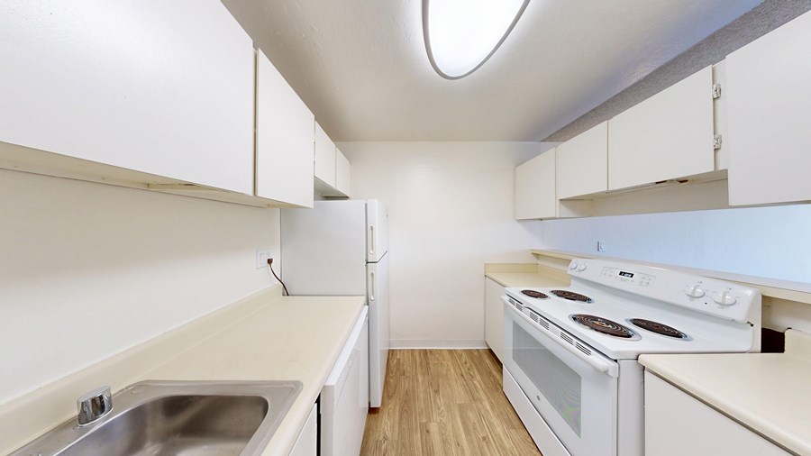 A white kitchen with a stove, sink, and cabinets.