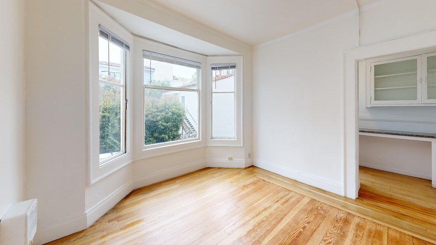 A room with wooden floors and white walls, with a window overlooking a green outdoor area.