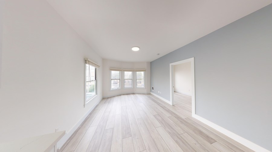 A spacious room with light wood flooring and white walls.