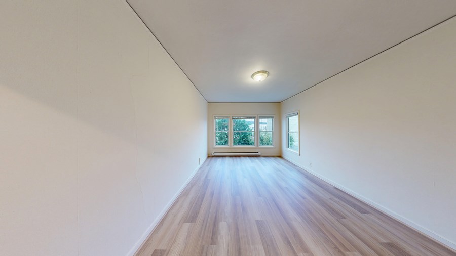 A long, empty room with wooden floors and a window at the end.