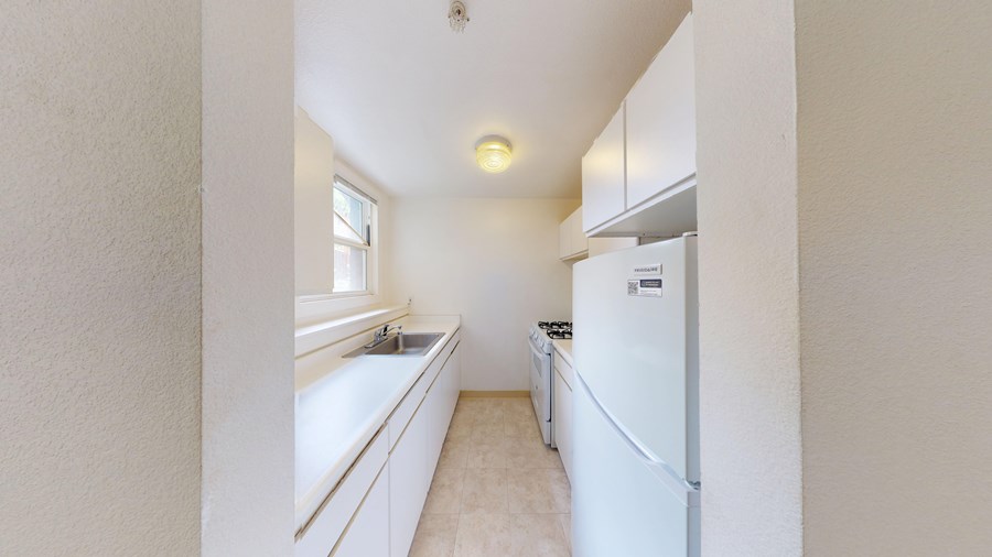 A white fridge sits in a kitchen with a sink and window.