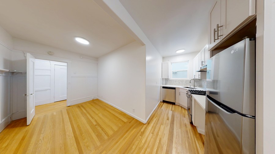 A kitchen with a refrigerator, sink, and wooden floors.