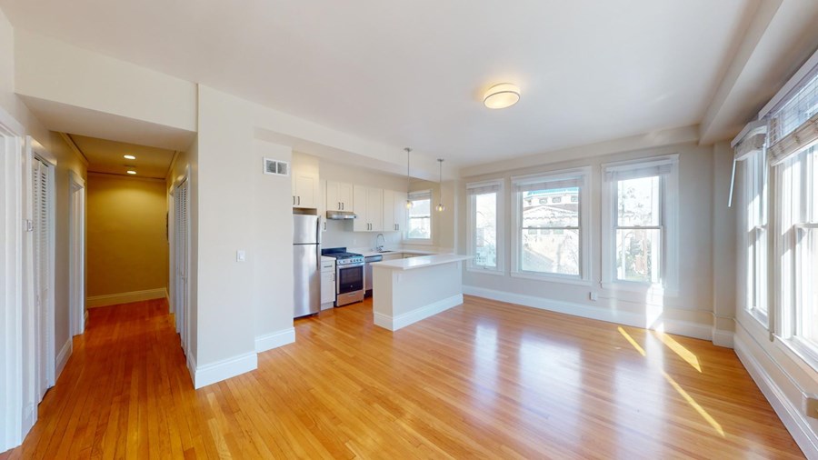A kitchen with white cabinets and a refrigerator is visible from the living room.