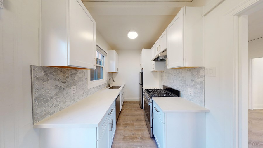 A kitchen with white cabinets and a marble backsplash.