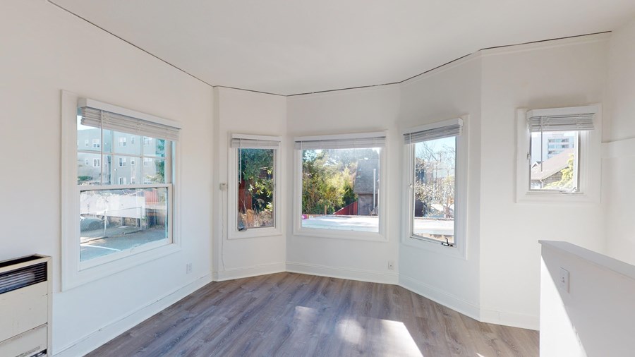 A room with white walls and wooden flooring, featuring three windows with views of the outside.