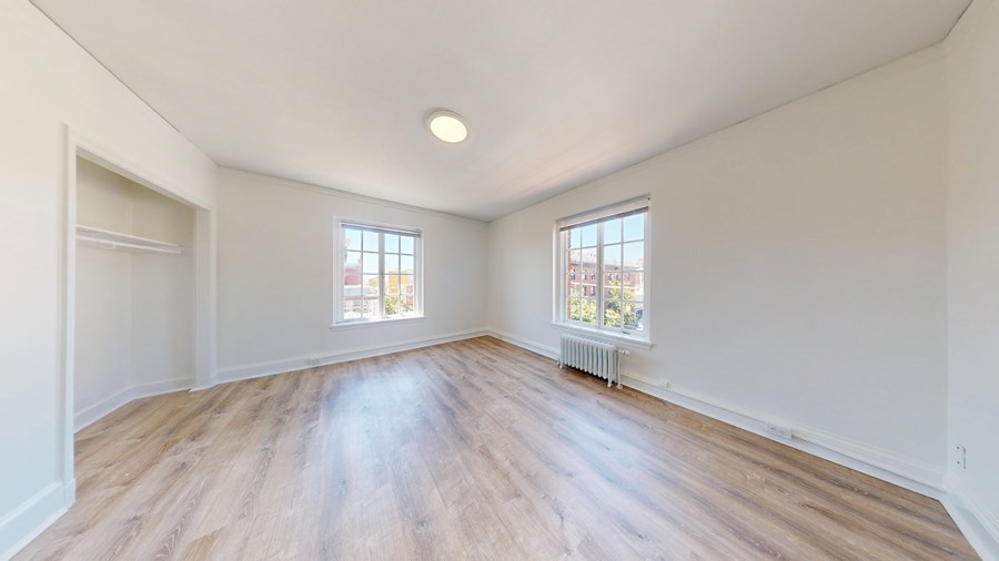 Empty room with wooden floors and two windows.