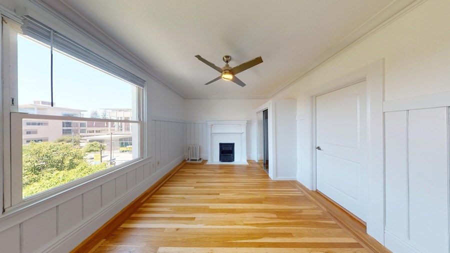 A long, empty room with wooden floors and a ceiling fan.