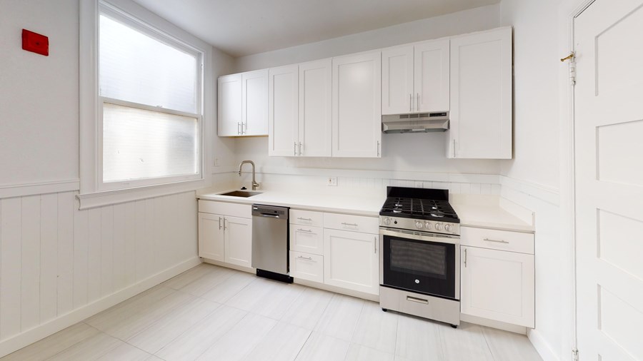 A white kitchen with a stove, sink, and cabinets.