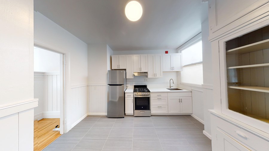 A kitchen with white cabinets and a grey floor.