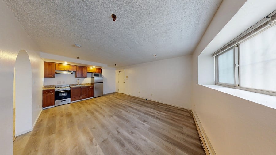 A room with wooden flooring and a kitchen area in the background.