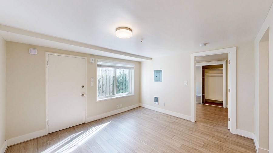 A room with white walls and wooden flooring, with a door on the left and an open door on the right.