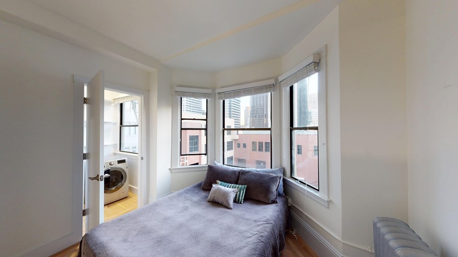 A bedroom with a bed, a couch, and a window overlooking a cityscape.
