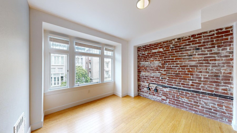 an empty living room with a brick wall and wood floors