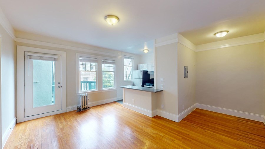 an empty living room with a kitchen and a window