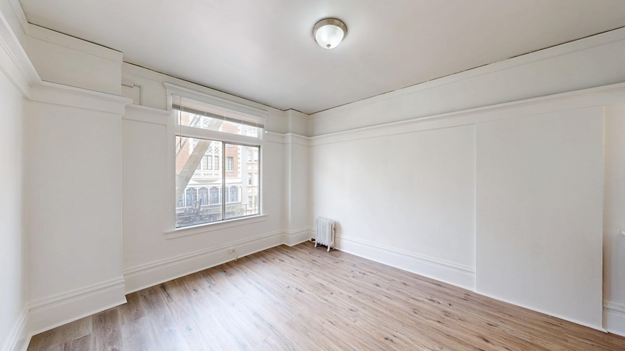 A room with white walls and wooden flooring with a window.