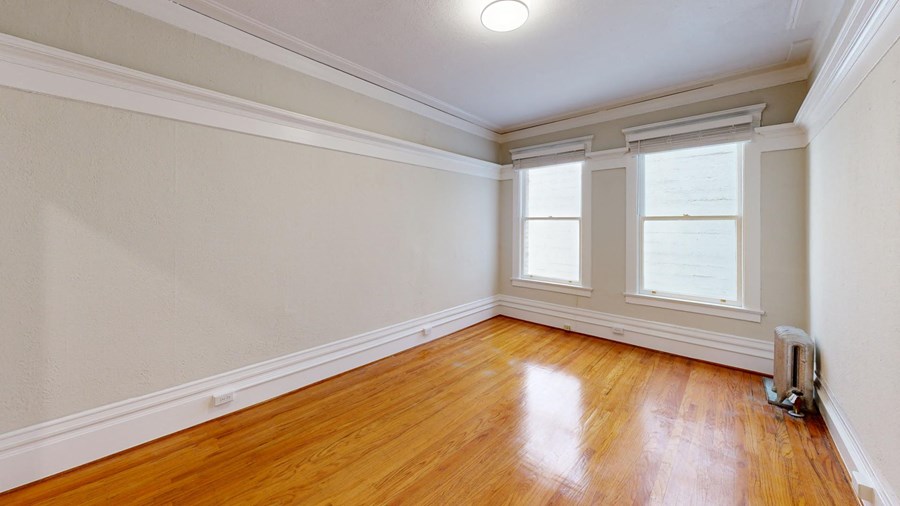 an empty room with wood floors and two windows