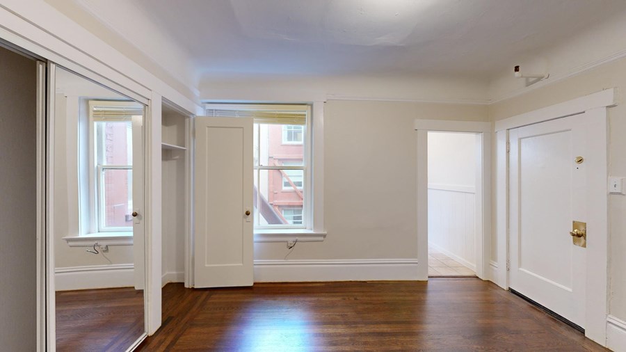A room with white walls and wooden floors, with a door on the right side.