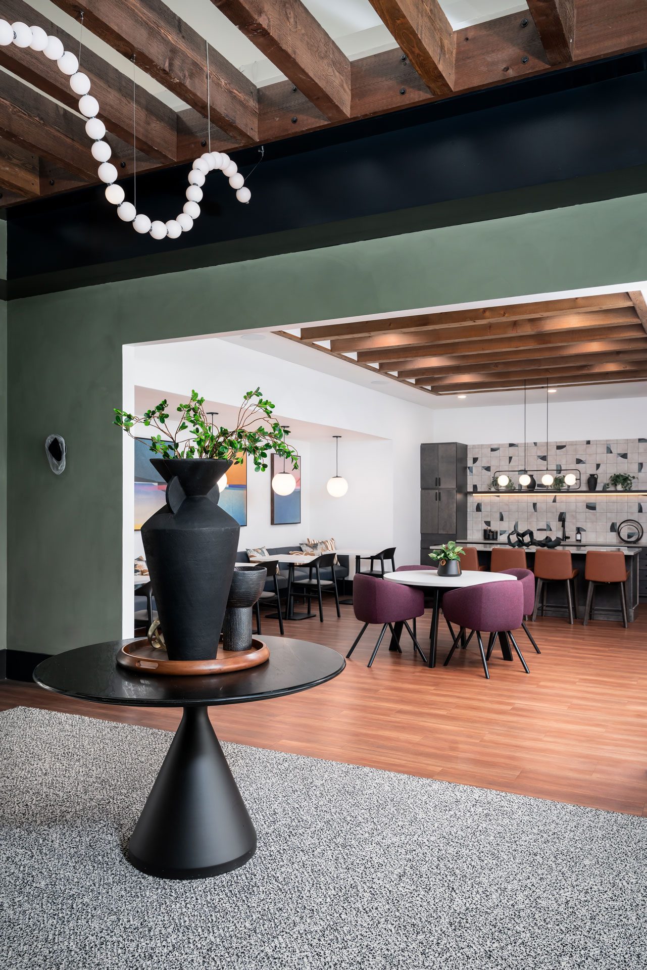 A black vase on a black pedestal with a grey carpet in front of a dining room.