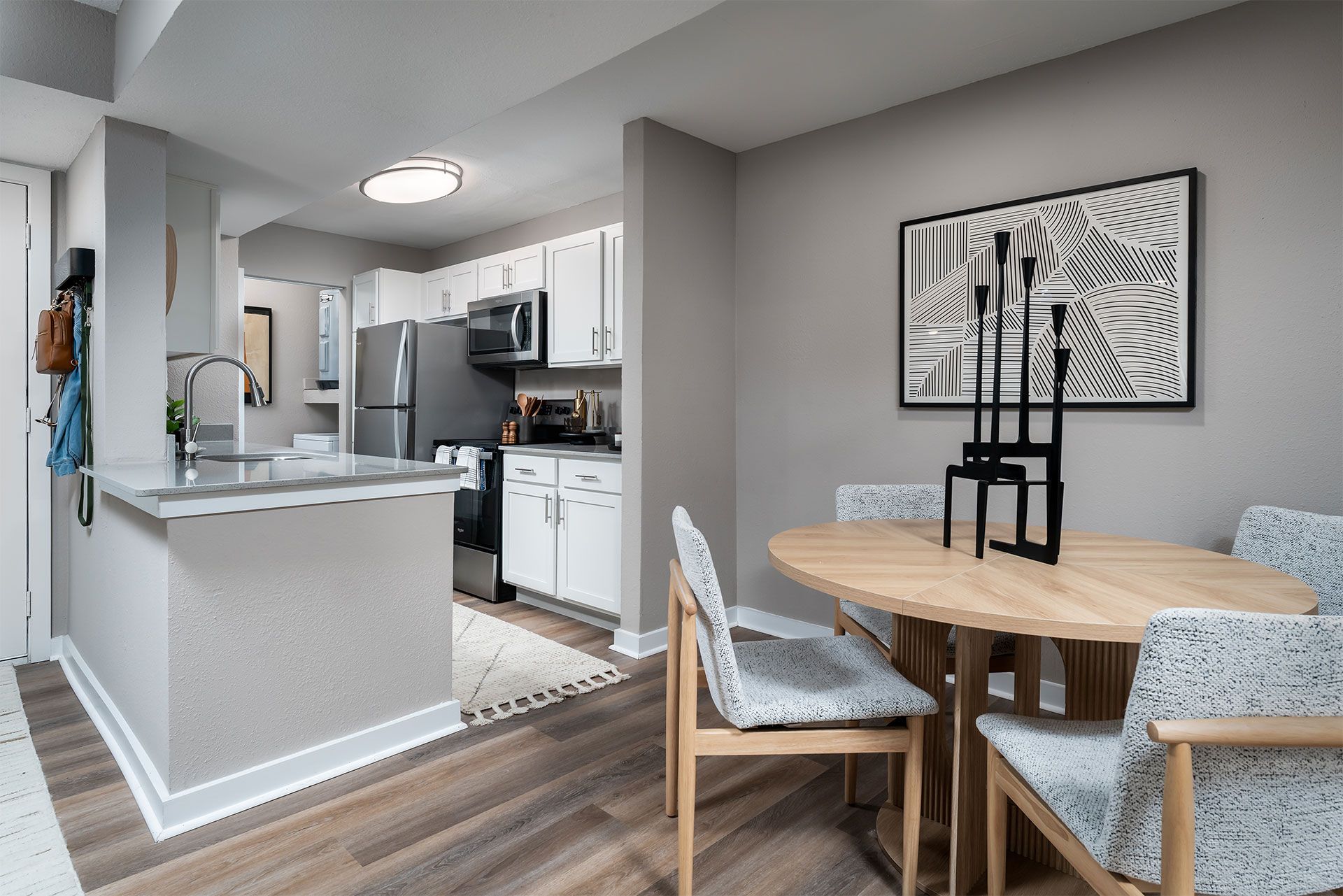 A kitchen with a table and chairs in the foreground and a fridge, microwave, and oven in the background.