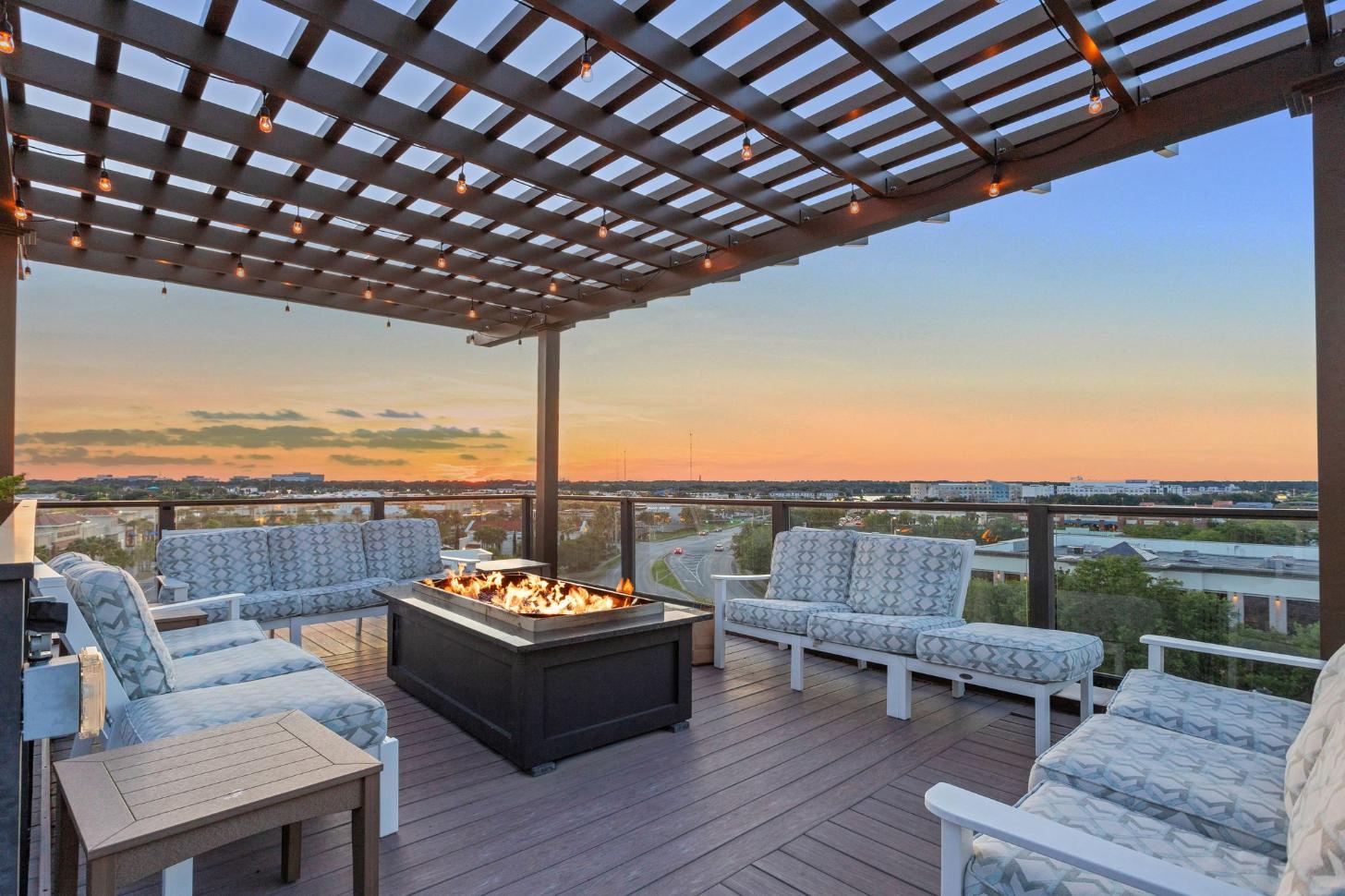 a patio with a fire pit on a roof overlooking a city at sunset
