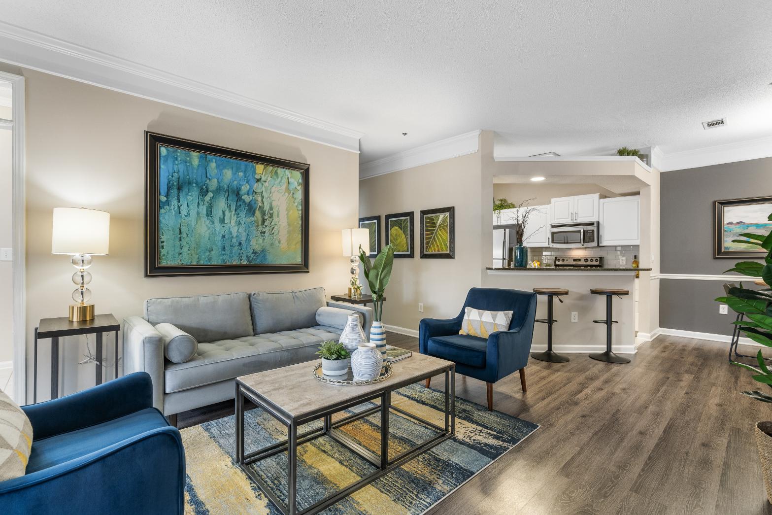 A living room with a blue armchair, a grey couch, a coffee table, and a painting on the wall.