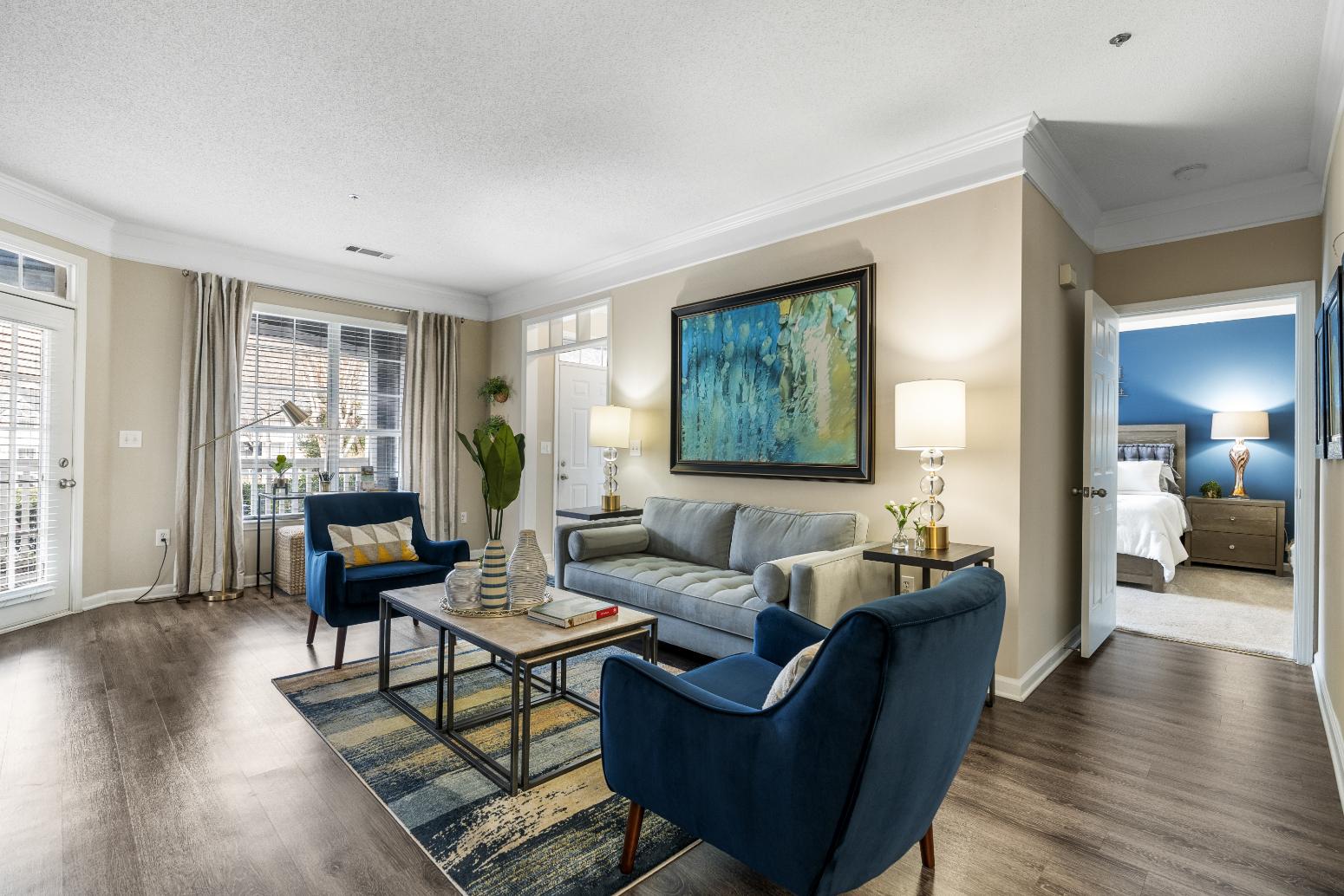 A living room with a blue chair and a painting on the wall.