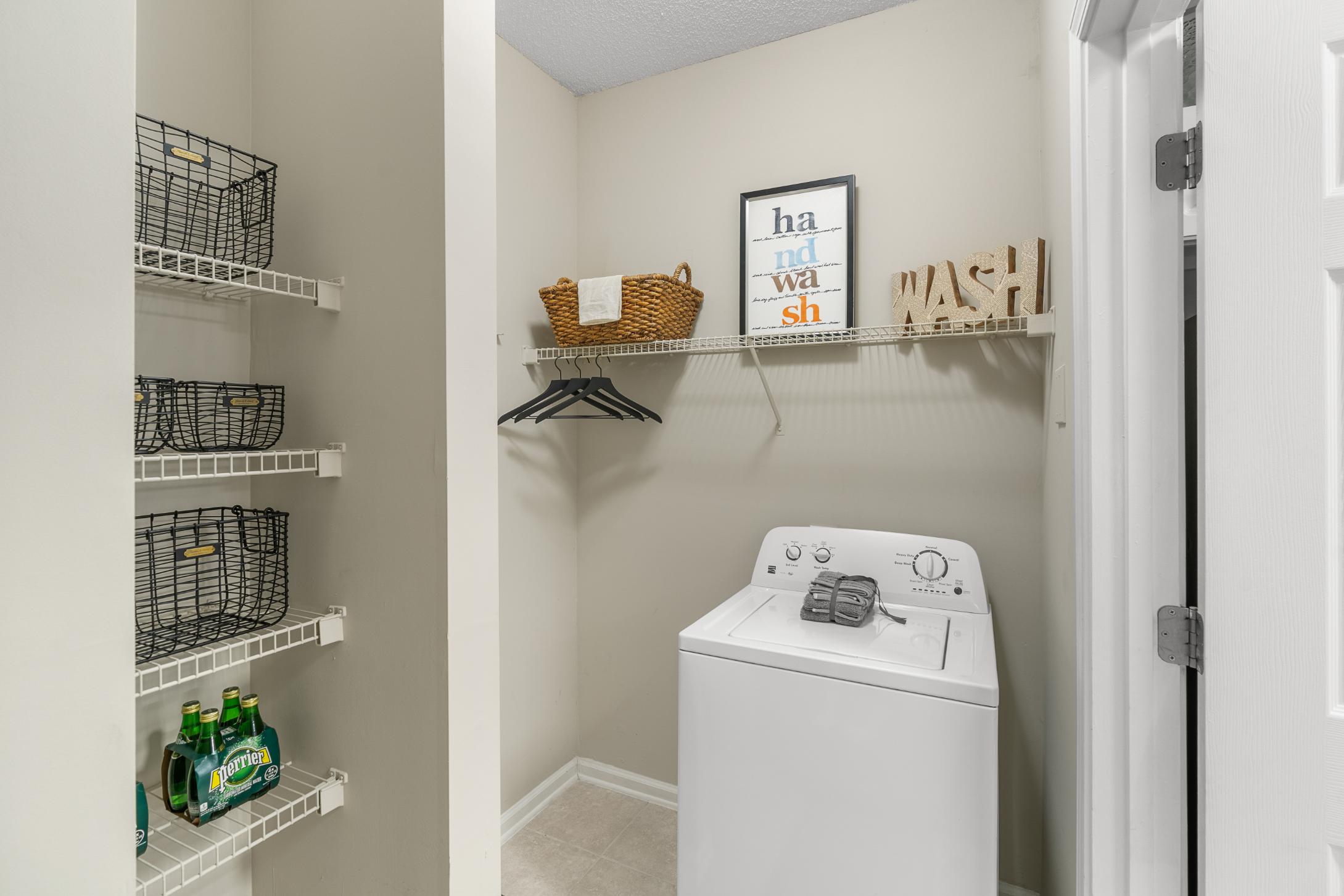 A laundry room with a washer and dryer and a shelf with a basket and a sign.