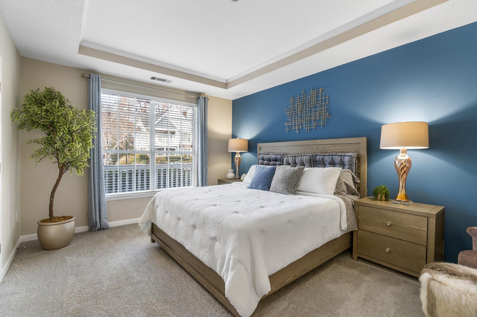 A bedroom with a bed, nightstand, and a potted plant.