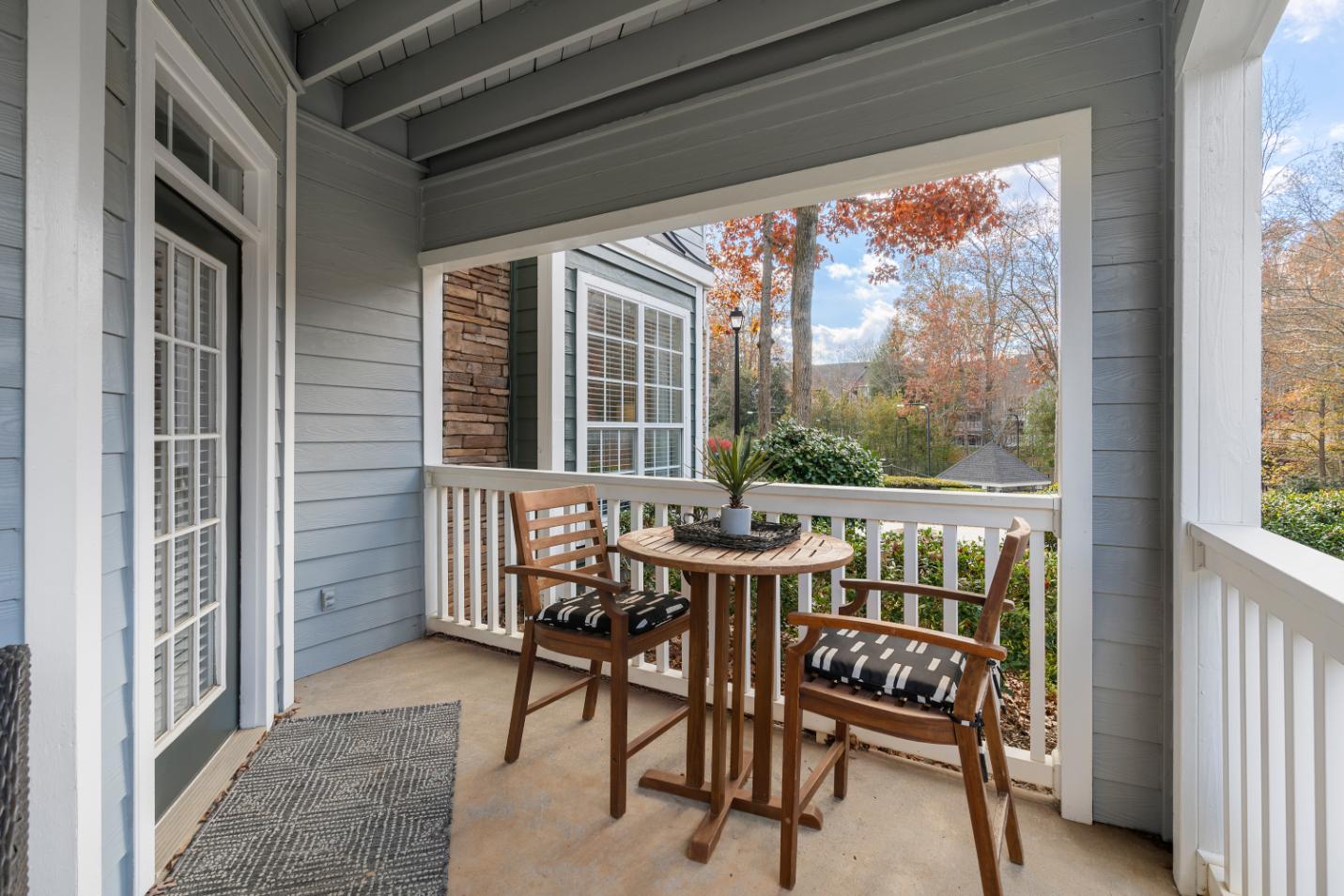 A wooden table and chairs are on a porch with a view of trees.