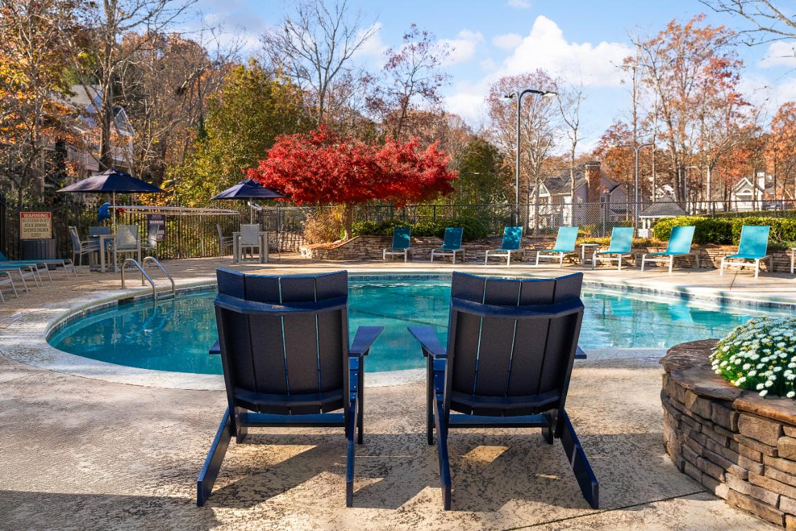 Two chairs are facing a pool with trees in the background.