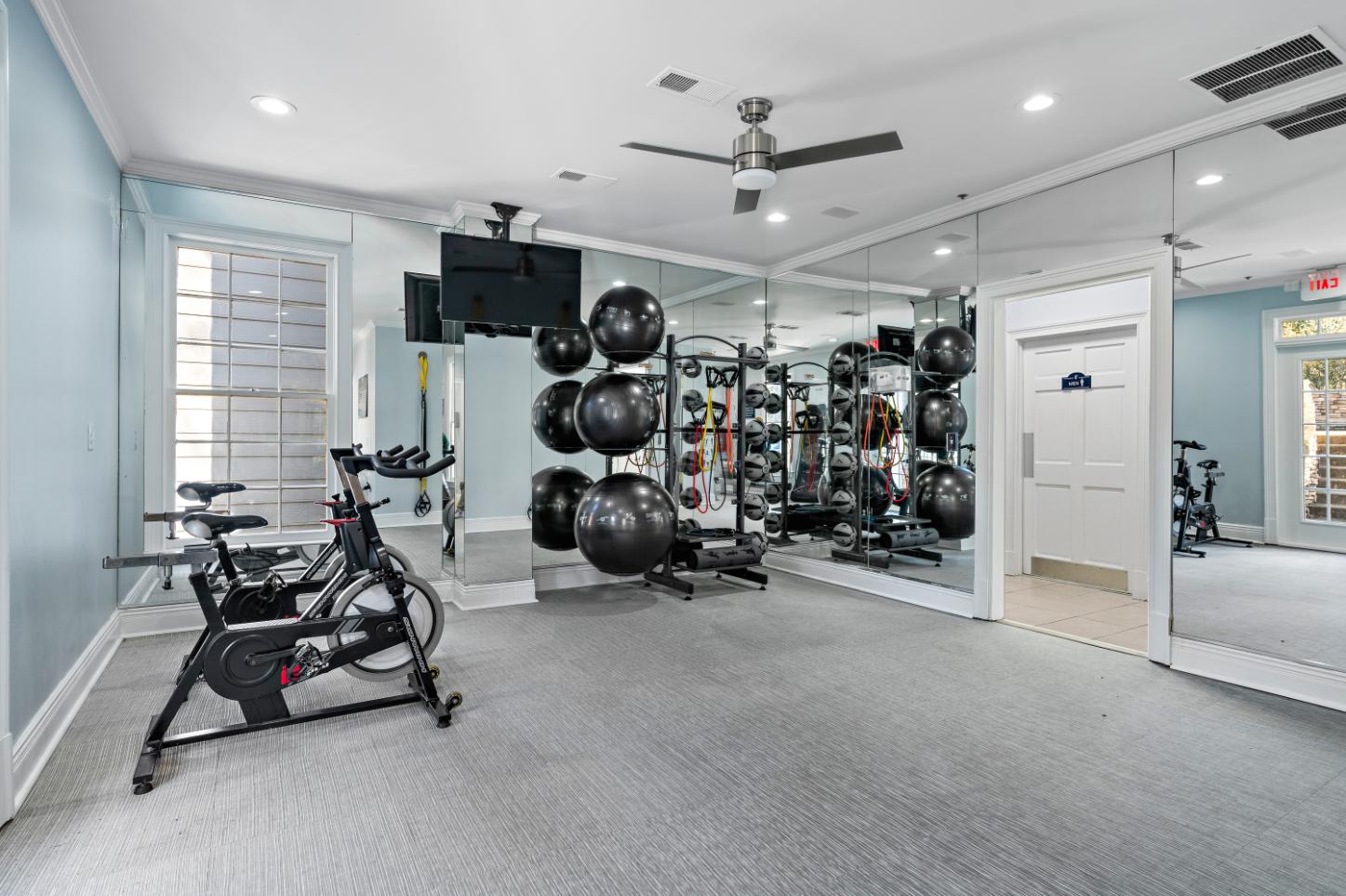 A spacious gym with a variety of exercise equipment including a stationary bike, a rowing machine, and a wall-mounted television.