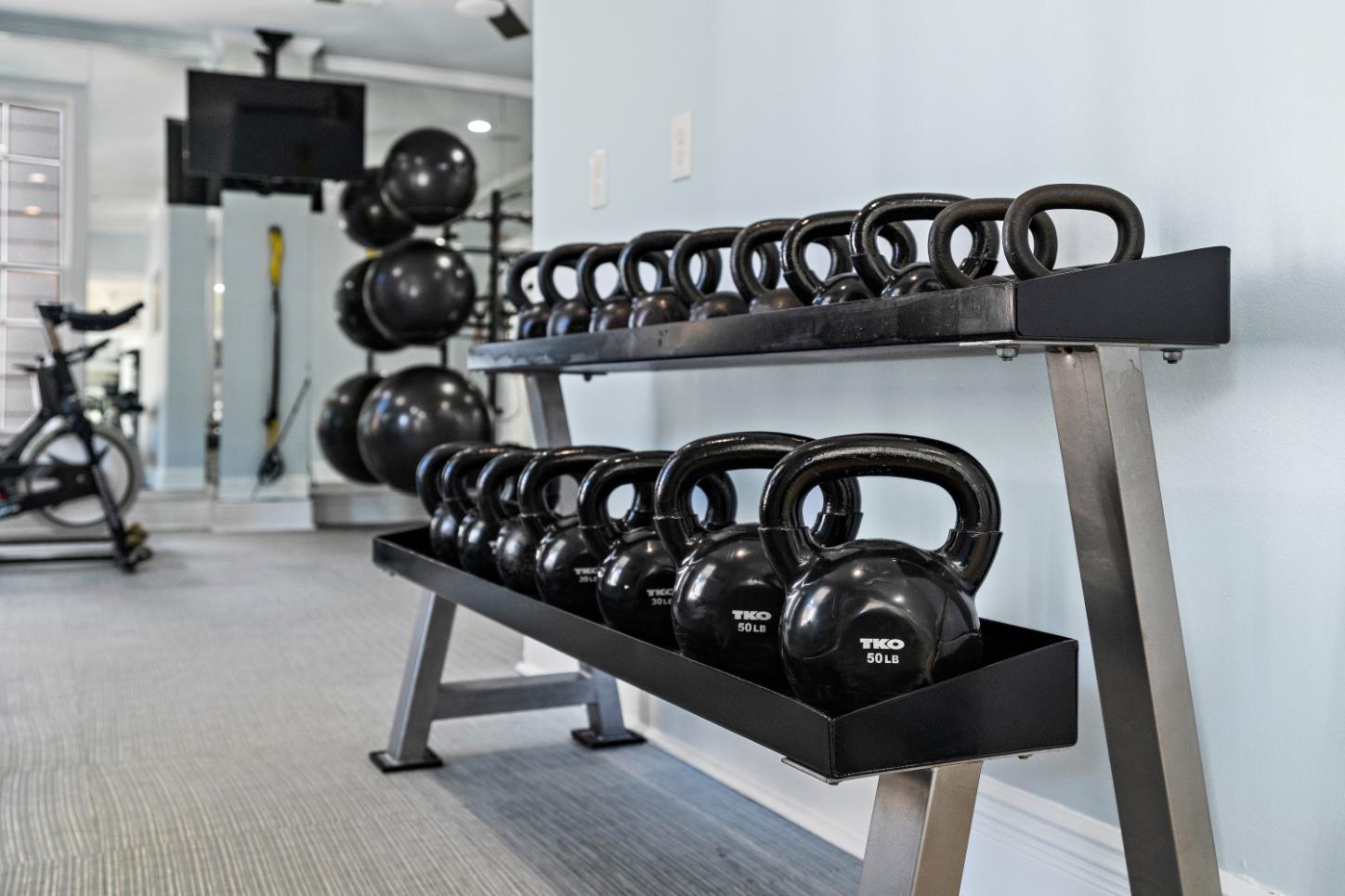 A row of kettlebells are lined up on a rack in a gym.