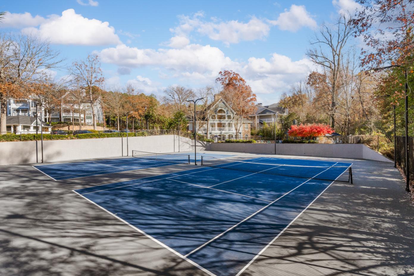 A tennis court surrounded by trees and a building in the background.