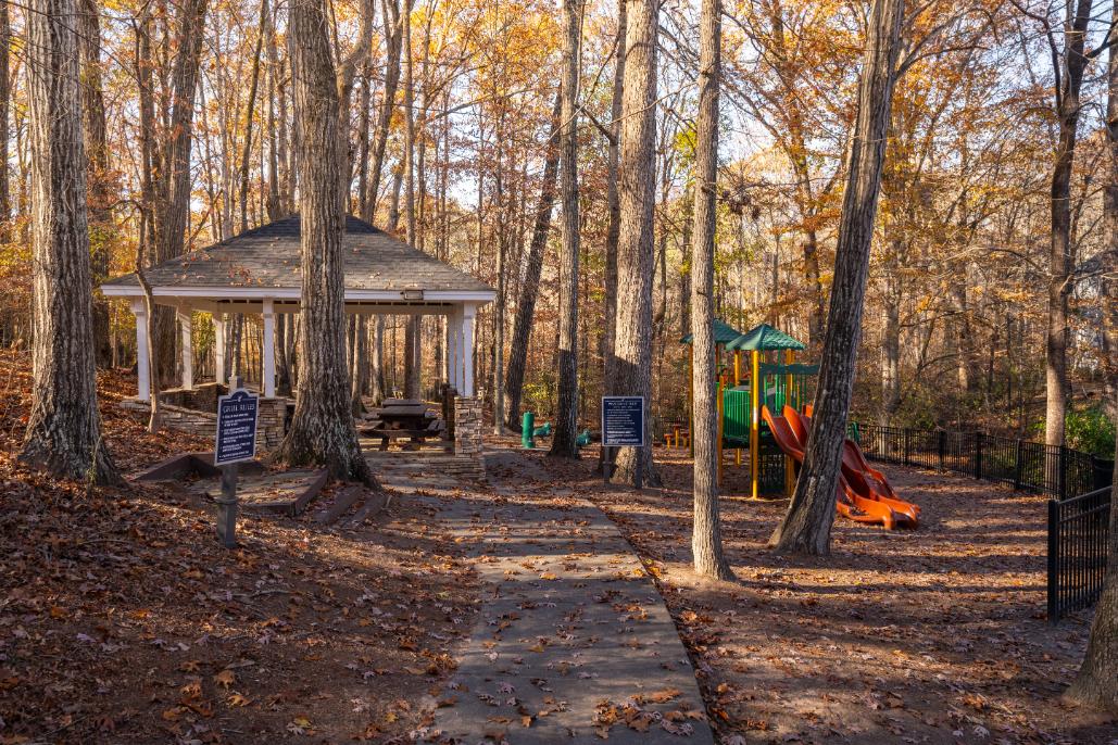 A gazebo sits in the middle of a playground surrounded by trees.