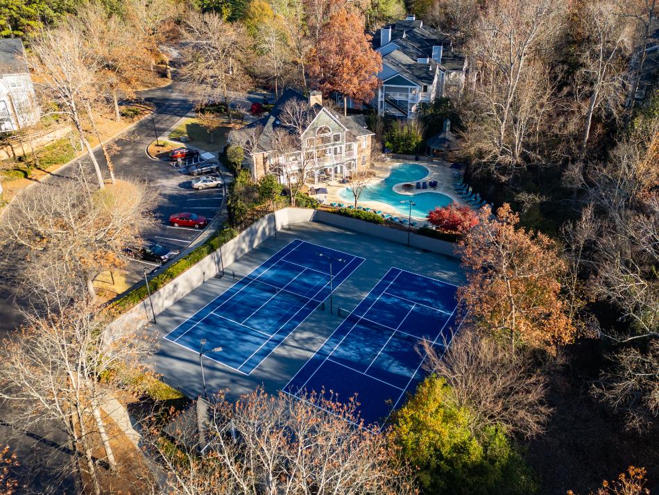 An aerial view of a tennis court surrounded by trees and a house.