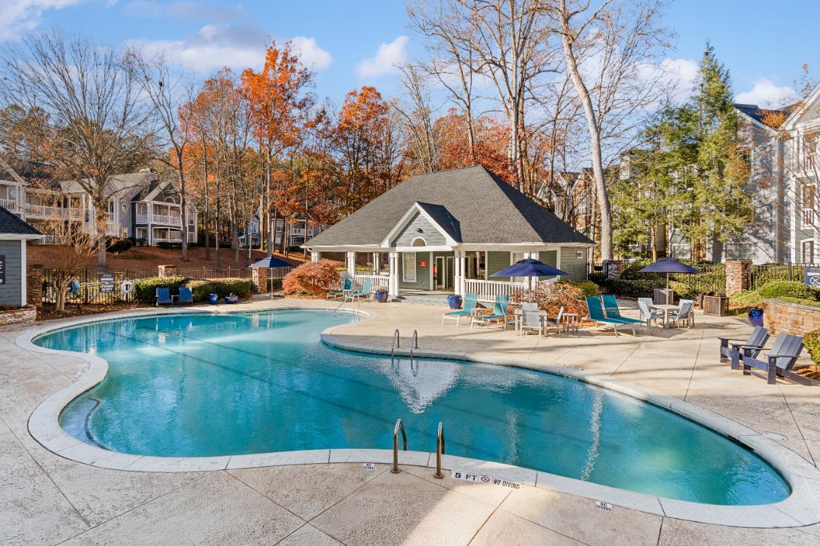 A large outdoor swimming pool surrounded by a patio area with chairs and umbrellas.