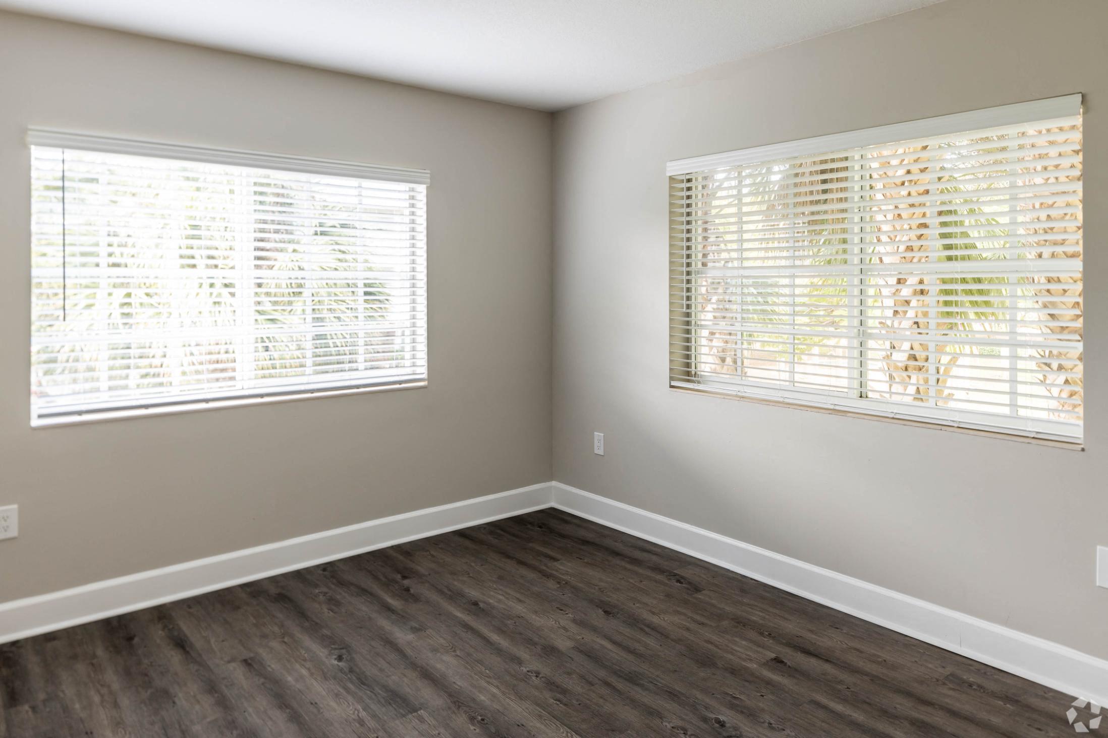 an empty room with wood floors and two windows