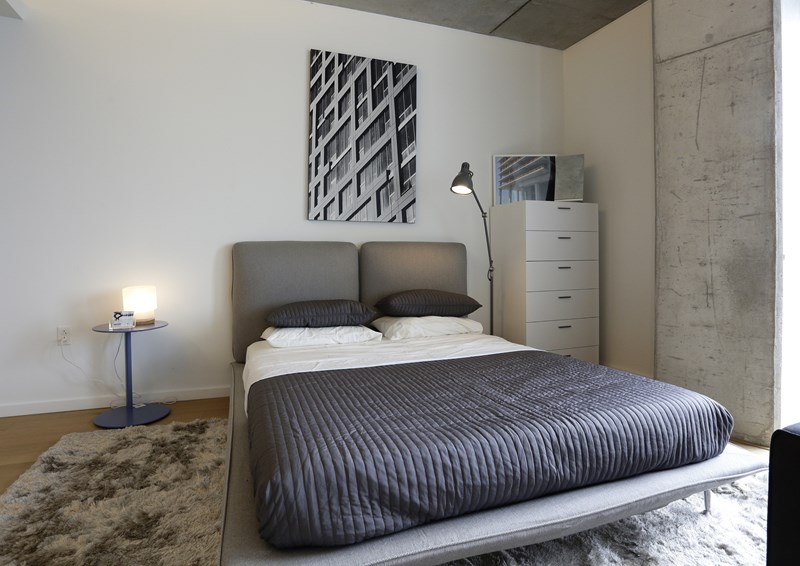 A bed with a grey cover and two pillows is in the center of the image.