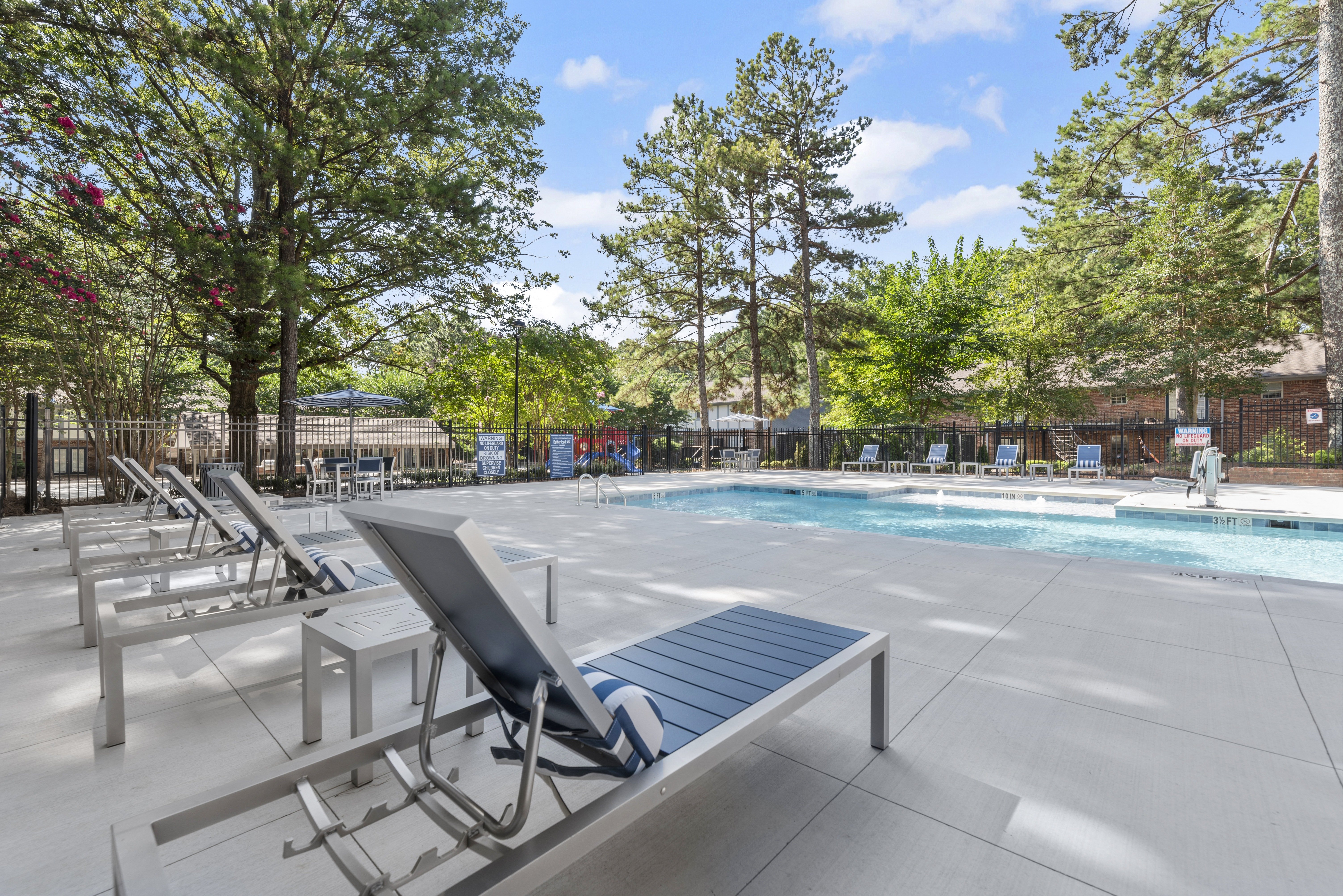 A pool area with sun loungers and trees.