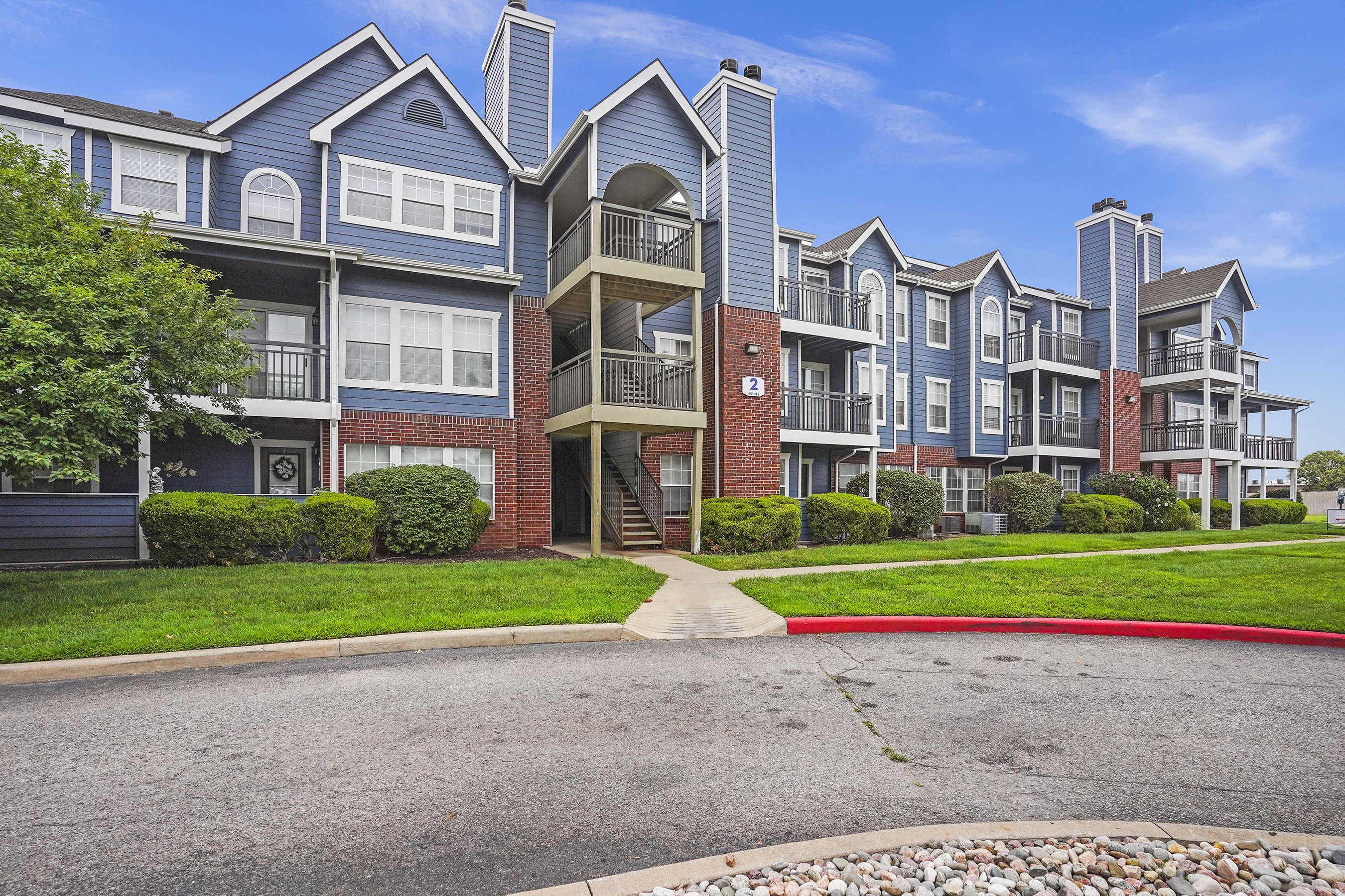 Apartment building with a red brick entrance and a small front yard.