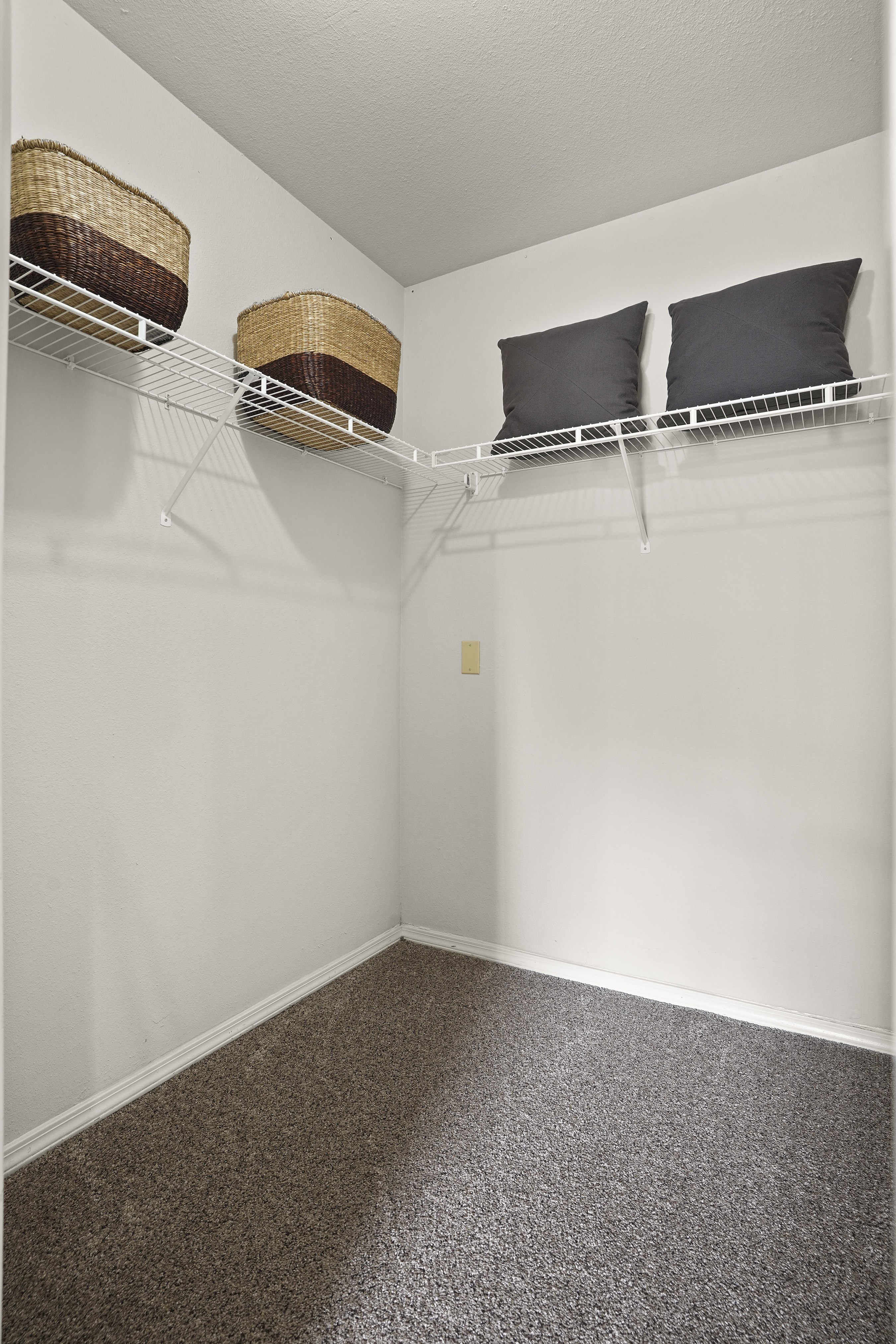 A white wall with a shelf and two pillows on it.