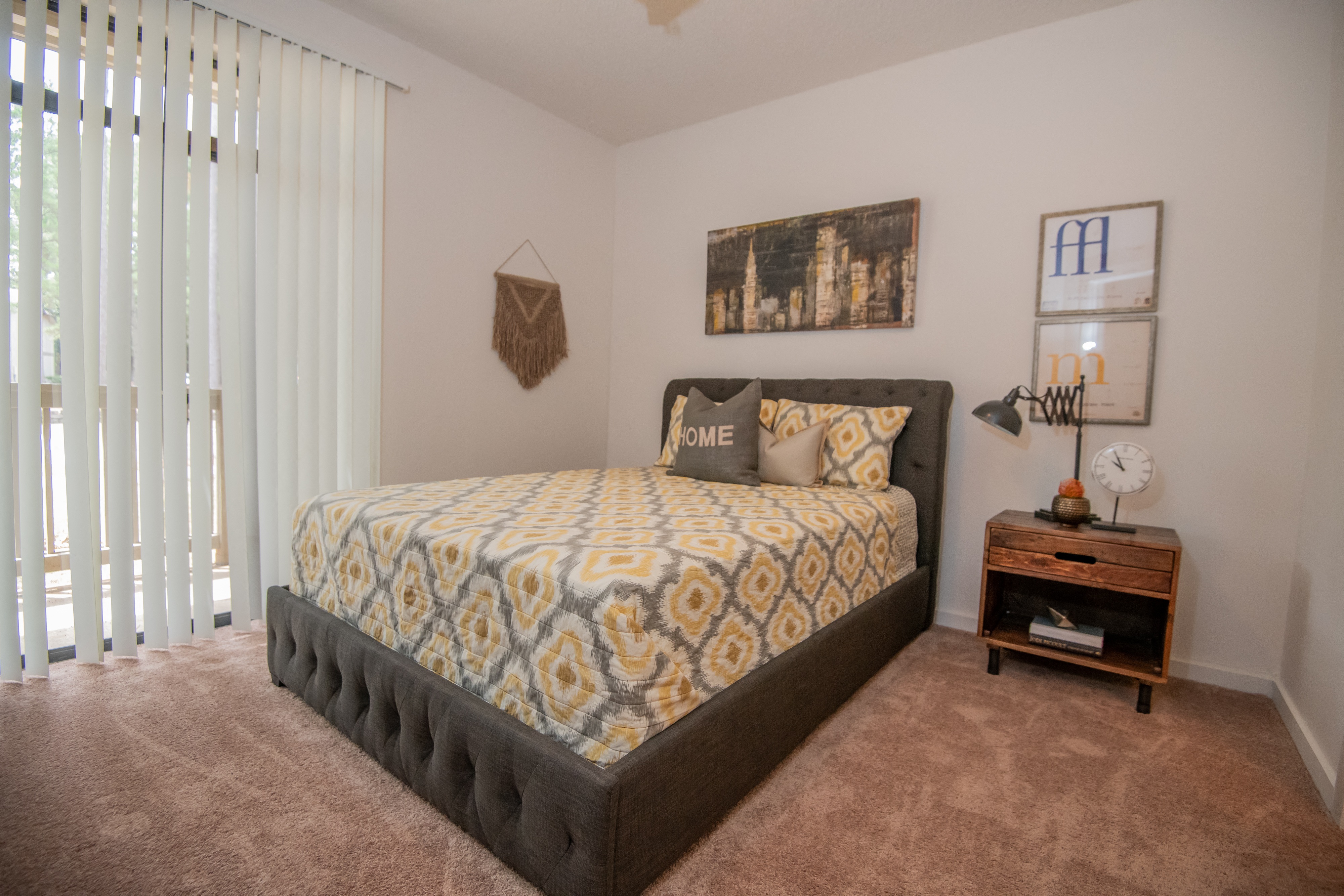 A bedroom with a large bed and a small table with a clock on it.
